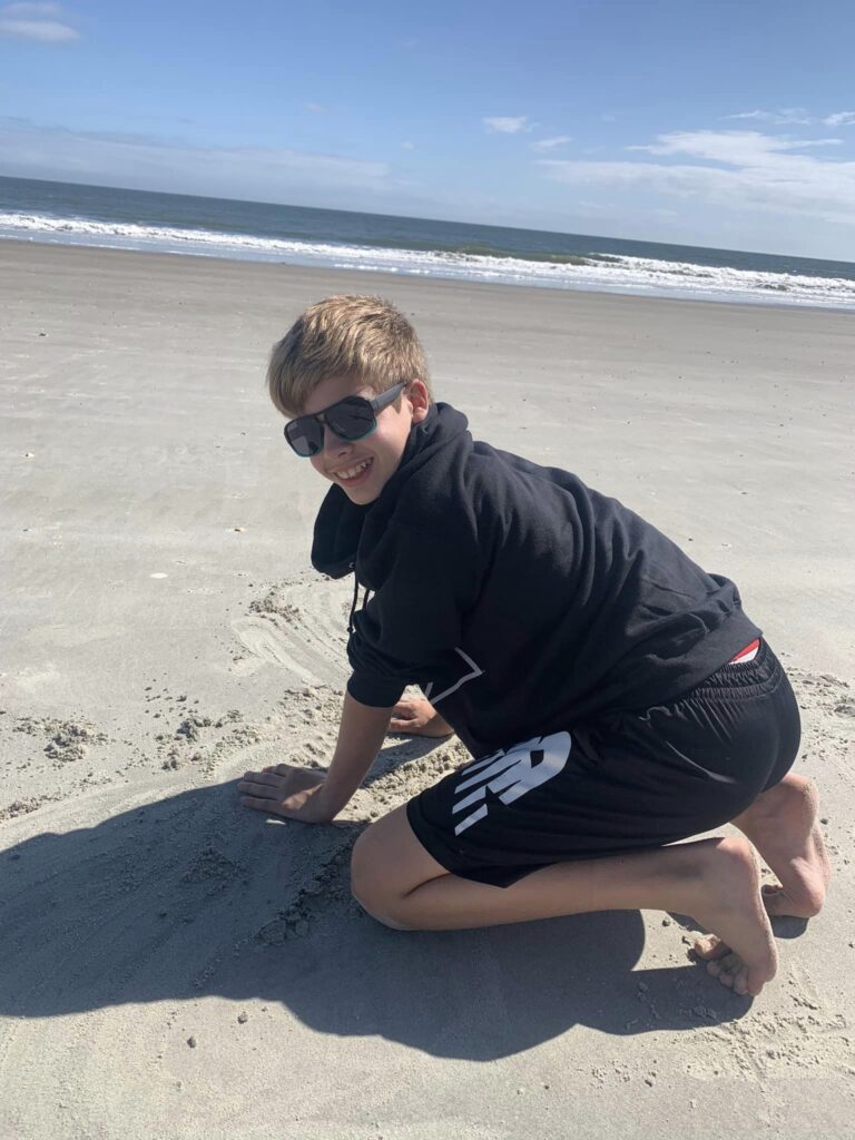 boy in sweatshirt playing in sand by the ocean