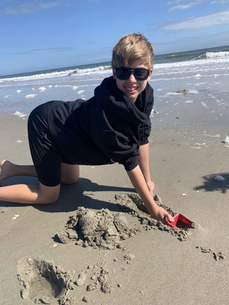 boy in sweatshirt playing in sand by the ocean