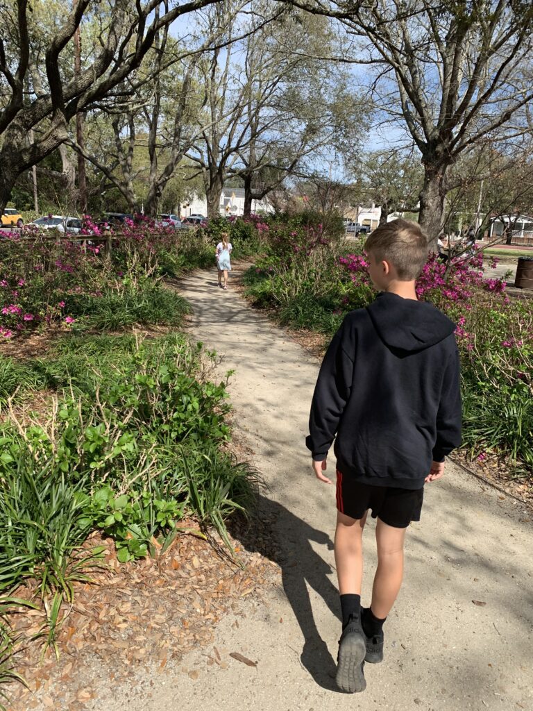 boy walking away from the camera down a garden path with a girl running farther ahead