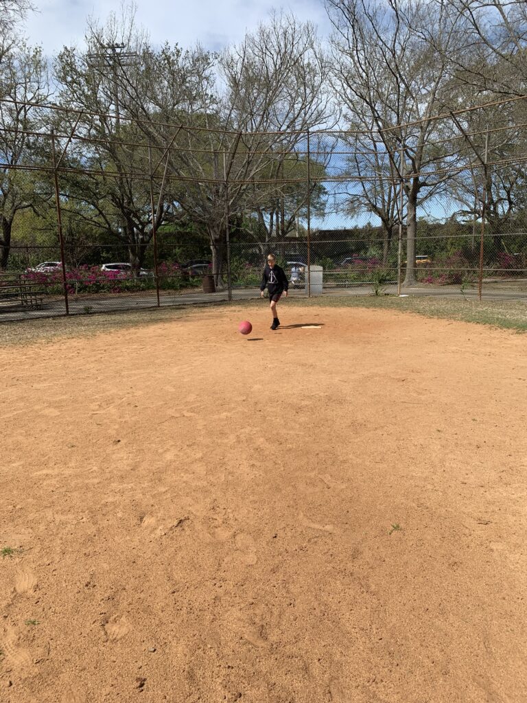 boy getting ready to kick a kickball on a baseball field