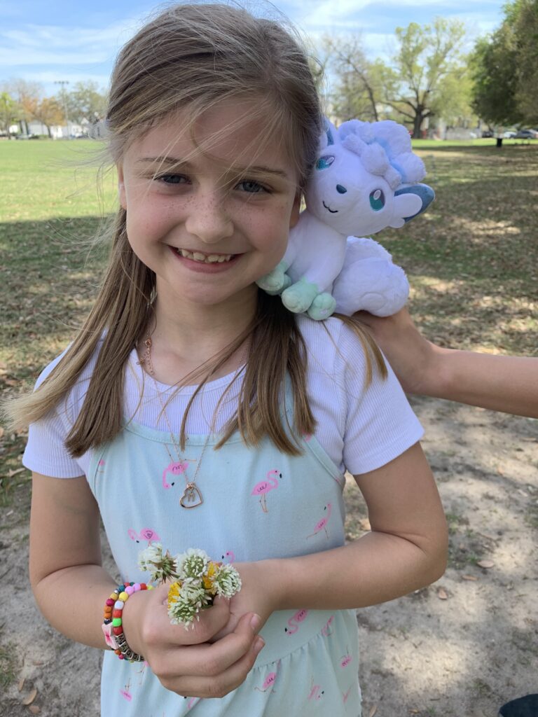 girl smiling for picture while a hand holds a stuffed animal on her shoulder